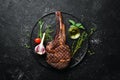 Grilled cowboy beef steak, herbs and spices on a black stone background. Barbecue. Top view. Royalty Free Stock Photo