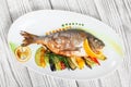 Grilled dorado fish with baked vegetables and rosemary on plate on wooden background close up.