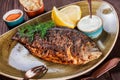 Grilled dorado fish with lemon and greens on plate on wooden background.