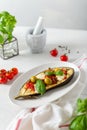 Grilled eggplant with mozzarella cheese, cherry tomatoes, olives and basil on white plate on a light background. Vertical, copy Royalty Free Stock Photo