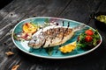 Grilled fish decorated with suce and citrus slices and tomato salad in a blue plate Royalty Free Stock Photo