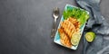 Grilled fish with fresh herbs and lime in a rectangular blue plate.