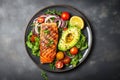 Grilled fish salmon steak and vegetables salad with avocado on ceramic plate on rustic stone background top view, balanced diet or Royalty Free Stock Photo