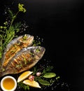 Grilled fish, sea bream with additions, herbs, olive oil, spices on a black background. Composition in the bottom left corner