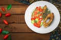 Grilled fish steak with vegetables on plate: tomatoes, microgran, cucumber, tasty and healthy dinner. Wooden rustic background. To Royalty Free Stock Photo