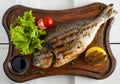 Grilled fish & x28;Dorado& x29; on a wooden board with lemon, salad, sauce and cherry tomatoes Royalty Free Stock Photo