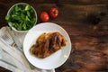 grilled half chicken with cutlery, salad and tomatoes on a rustic wooden background with copy space, top view from above