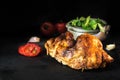 Grilled half chicken on a dark slate plate with salad and tomato