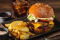 Grilled hamburger with double cutlet, fries in a metal bowl and cola on a wooden table. Hamburger and French fries.