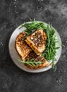Grilled hot sandwiches with beans, tomato sauce, cheddar cheese and arugula salad on a dark background, top view Royalty Free Stock Photo