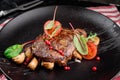 Grilled juicy steak with grilled mushrooms, tomatoes and cranberries on a dark plate and rad napkin on a dark background Royalty Free Stock Photo