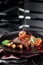 Grilled juicy steak with grilled mushrooms, tomatoes and cranberries on a dark plate and rad napkin on a dark background Royalty Free Stock Photo