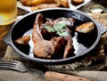 Grilled lamb chops with garlic and herbs in a pan, vintage fork, a glass of beer in the background Royalty Free Stock Photo