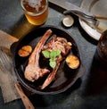 Grilled lamb chops with garlic and herbs in a pan, vintage knife and fork, a glass of beer in the background Royalty Free Stock Photo