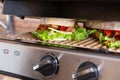 Grilled long sandwich or panini on the grill of an electric grill. Crisp bread, lettuce, tomato, cheddar, salsa sauce -