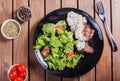 Grilled meat with fresh vegetable salad and tomatoes on black plate, wooden background Royalty Free Stock Photo