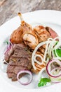 Grilled meat on plate, chicken legs, beef steak and onion on wooden background close up