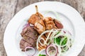 Grilled meat on plate, chicken legs, beef steak and onion on wooden background close up. Top view.