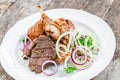 Grilled meat on plate, chicken legs, beef steak and onion on wooden background close up.