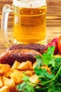 Grilled meat sausages with fried potatoes, fresh produce and mug of beer on wooden board Royalty Free Stock Photo