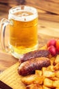 Grilled meat sausages with fried potatoes, fresh produce and mug of beer on wooden board Royalty Free Stock Photo