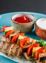 Grilled meat shish and vegetables kebab on skewers with sauce in plate over dark background. Healthy food. Hot meat dishes, Royalty Free Stock Photo