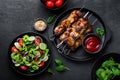 Grilled meat skewers, shish kebab and healthy vegetable salad of fresh tomato, cucumber, onion, spinach, lettuce and sesame on bla Royalty Free Stock Photo