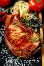 Grilled meat on a stone board. Appetizing Pork steak with herbs and spices. Close-up. Dark wooden background. Vertical shot Royalty Free Stock Photo