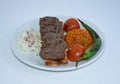 Close up of grilled meatballs, bulgur pilaf, roasted tomatoes and peppers served on white plate