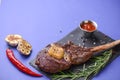 Grilled Medium rare barbecue Steak on bone with spices served on a rustic wooden board with sauce over blue background. Royalty Free Stock Photo