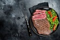 Grilled medium rare flank beef steak with salad in a plate. Black background. Top view. Copy space Royalty Free Stock Photo