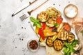 Grilled multicolored vegetables, aubergines, zucchini, pepper with green basil on serving stone board on gray background, top view