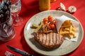 Grilled New York strip steak with bearnaise sauce, potato wedges, and cherry truss tomatoes. Garnished with parsley and