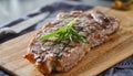 Grilled new york strip steak resting on wooden cutting board with rosemary garnish