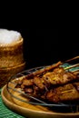 Grilled pork on bamboo skewers placed on a steel grill in a wooden tray with sticky rice in the cart, ready to serve Royalty Free Stock Photo