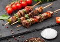 Grilled pork and chicken kebab with paprika on stone chopping board with salt, pepper and tomatoes on black background Royalty Free Stock Photo