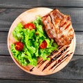 Grilled pork chop steak with fresh vegetable salad, tomatoes and sauce on wooden cutting board. Royalty Free Stock Photo