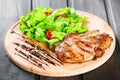 Grilled pork chop steak with fresh vegetable salad, tomatoes and sauce on wooden cutting board. Hot Meat Dishes