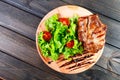 Grilled pork chop steak with fresh vegetable salad, tomatoes and sauce on wooden cutting board. Hot Meat Dishes.