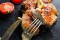 Grilled pork chop with tomatoes top view with knife and slice on fork over black Dish close up