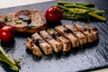 Grilled pork chops, steaks with vegetables, tomatoes, beans and sauce on a black slate. Fresh meat with foam. Dark background. Gri