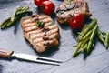 Grilled pork chops, steaks with vegetables, tomatoes, beans and sauce on a black slate. Fresh meat with foam. Dark background. Gri