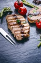 Grilled pork chops, steaks with vegetables, tomatoes, beans and sauce on a black slate. Fresh meat with foam. Dark background. Gri