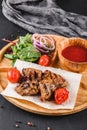 Grilled pork meat and vegetables with fresh salad and bbq sauce on cutting board over black stone background. Hot Meat Dishes Royalty Free Stock Photo