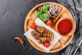 Grilled pork meat and vegetables with fresh salad and bbq sauce on cutting board over black stone background Royalty Free Stock Photo