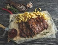 Grilled pork ribs with sauce on a cutting board, french fries, spices, wooden background Royalty Free Stock Photo