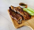 Grilled pork ribs, sliced cucumber and spicy sauce on wooden tray. Close up Barbecue food with fresh vegetables on white marble Royalty Free Stock Photo