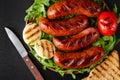 Grilled pork sausages with arugula and vegetables on black background.