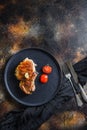 Grilled pork steak on the bone with seasonings on black dish with sfork and knife on cloth, over rustic metall surface overhead Royalty Free Stock Photo