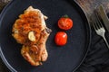 Grilled pork steak on the bone with seasonings on black dish with sfork and knife on cloth, over rustic metall surface top view Royalty Free Stock Photo